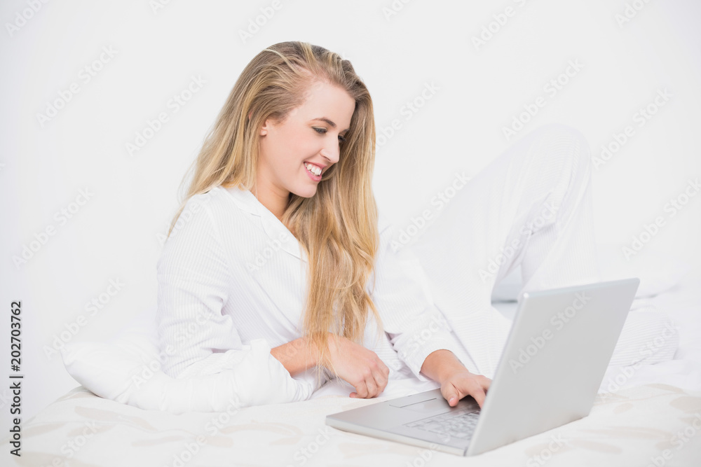 Smiling pretty model using her laptop lying on cosy bed Smiling pretty model using her laptop lying on cosy bed