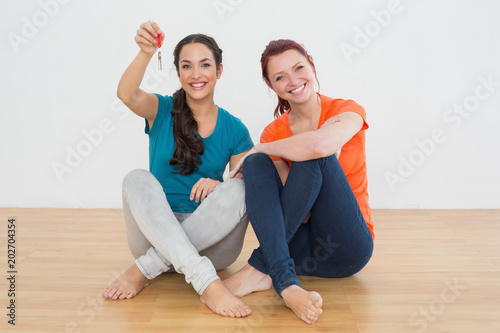 Female friends with house keys sitting on the floor