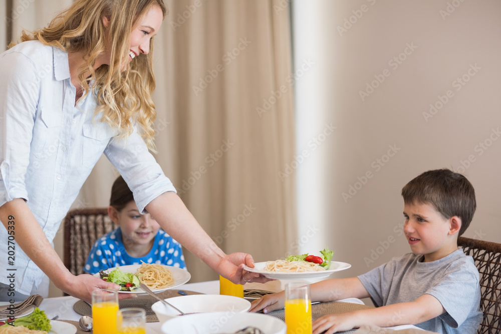 Mother serving pasta to son at dining table