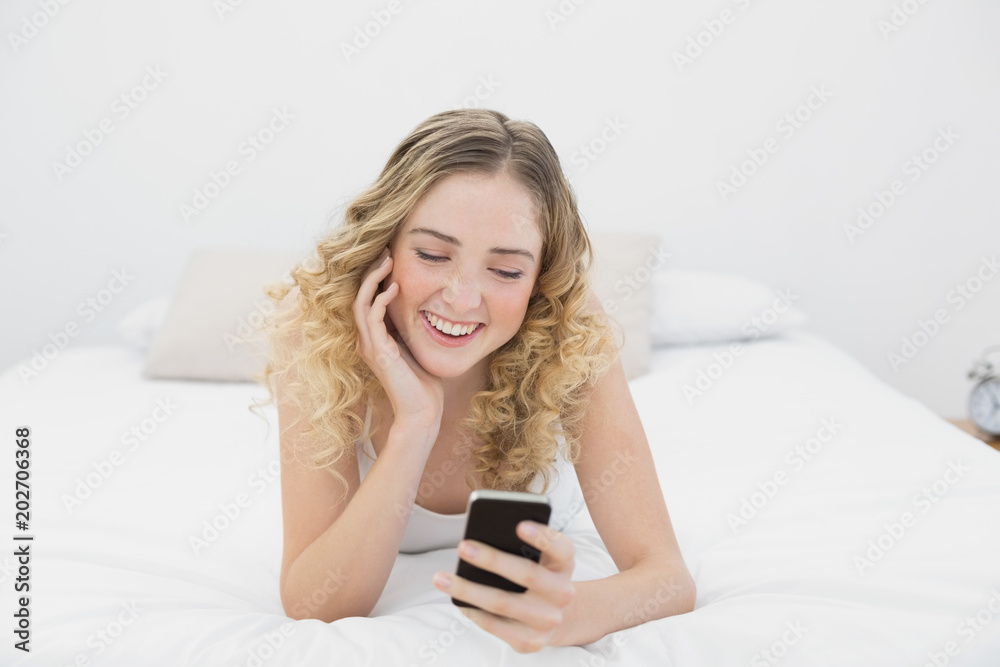 Pretty smiling blonde lying on bed using smartphone Pretty smiling blonde lying on bed using smartphone