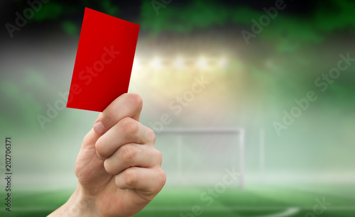 Hand holding up red card against football pitch under spotlights