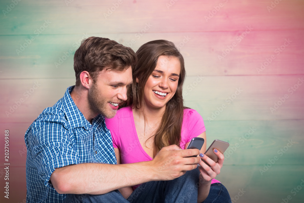 Cheerful couple with mobile phones against pink and green planks Cheerful couple with mobile phones against pink and green planks