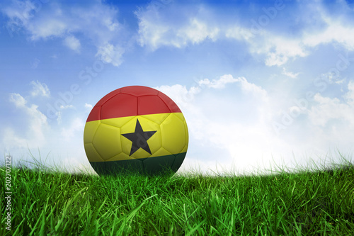 Football in ghana colours on field of grass under blue sky