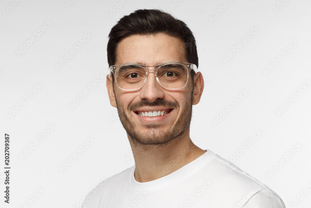 Studio portrait of confident European Caucasian man pictured isolated on gray background wearing casual clothes and plastic safety glasses showing happy friendly smile, willing to communicate Studio portrait of confident European Caucasian man pictured isolated on gray background wearing casual clothes and plastic safety glasses showing happy friendly smile, willing to communicate