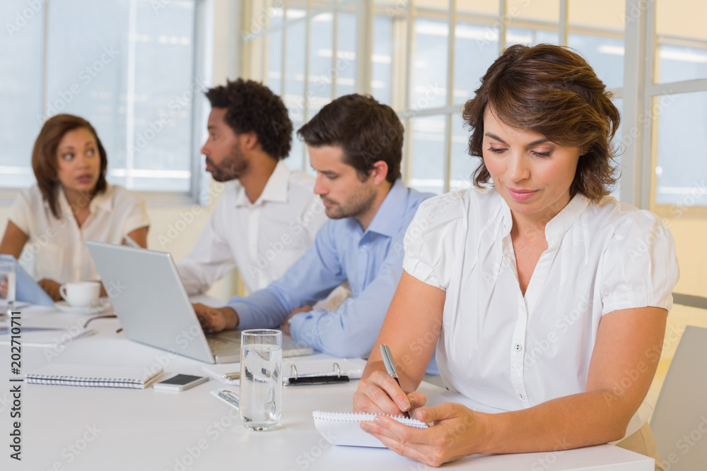 Fototapeta premium Businesswoman writing notes with colleagues in meeting at office