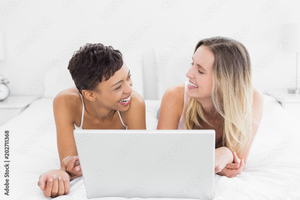 Cheerful female friends with laptop in bed