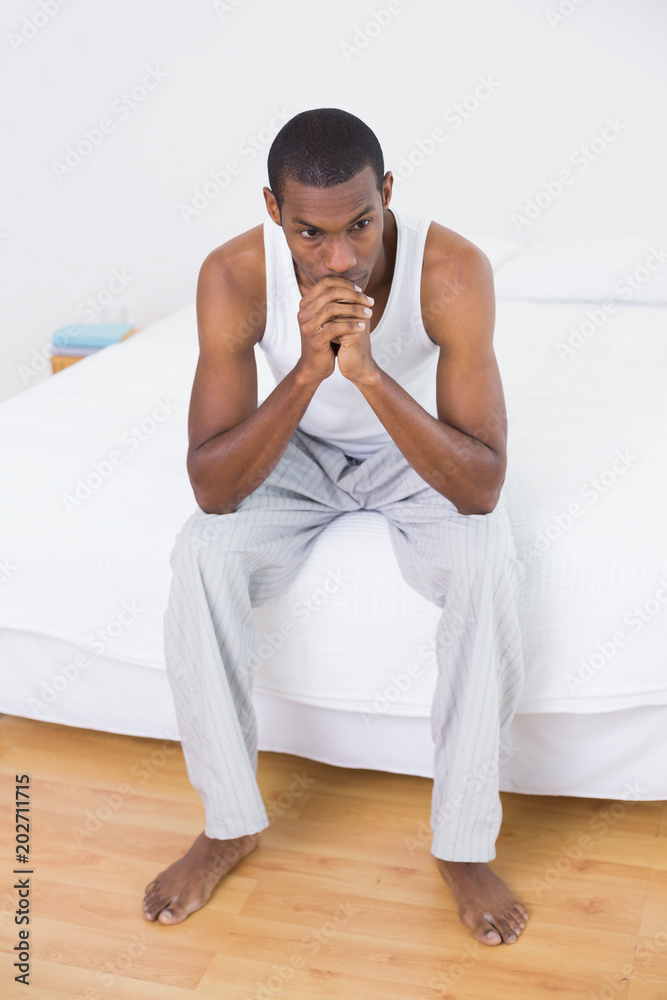 Thoughtful young Afro man sitting on bed