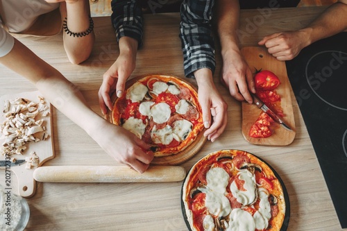 Friends cooking homemade pizza together, top view