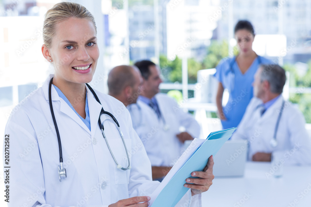 Smiling female doctor looking at camera while her colleages works Smiling female doctor looking at camera while her colleages works