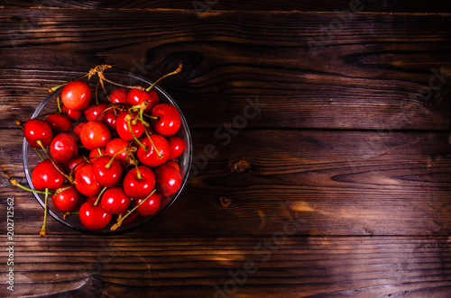 Fresh ripe cherries in glass bowl on wooden table. Top view