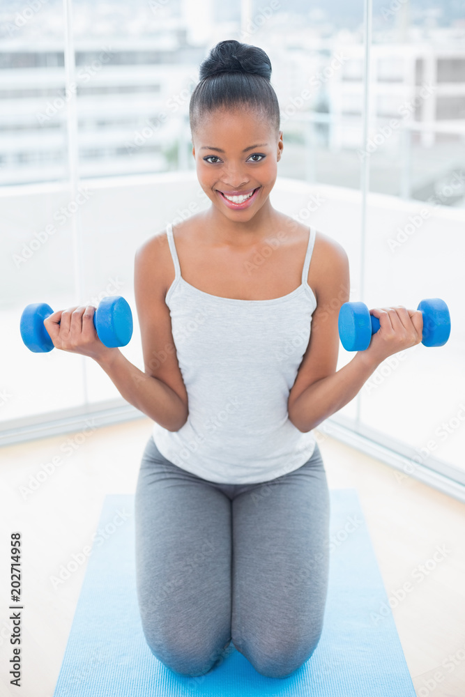 Fit woman sitting on exercise mat and working out with dumbbells Fit woman sitting on exercise mat and working out with dumbbells