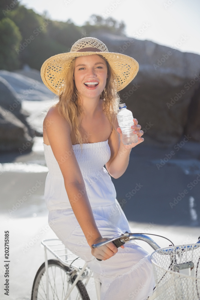Φωτογραφία Beautiful blonde in sundress on bike holding water bottle at the beach