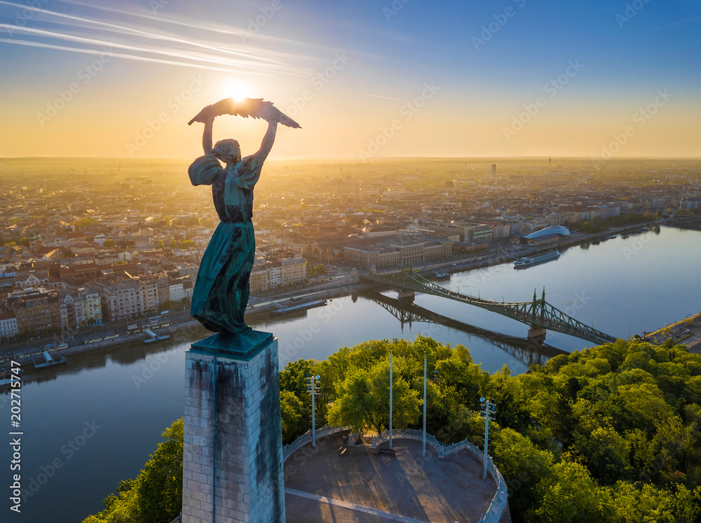 Naklejka premium Budapeszt, Węgry - Widok z lotu ptaka na piękną węgierską Statuę Wolności z Mostem Wolności i panoramę Budapesztu o wschodzie słońca z czystym błękitnym niebem