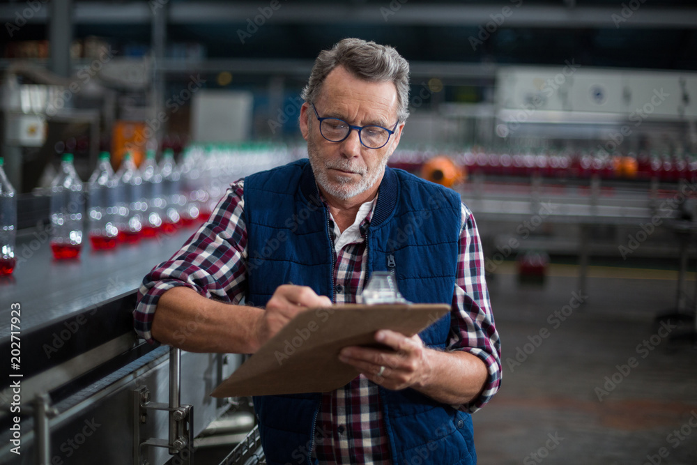 Male factory worker maintaining record on clipboard - obrazy, fototapety, plakaty 