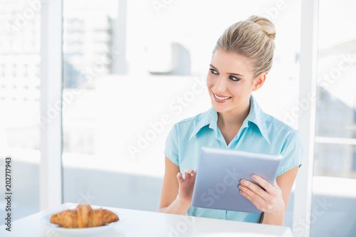 Cheerful classy woman using tablet while having breakfast