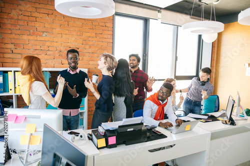 sad African guy cannot work on laptop because of noisy colleagues in the small office. draw worker away from his work