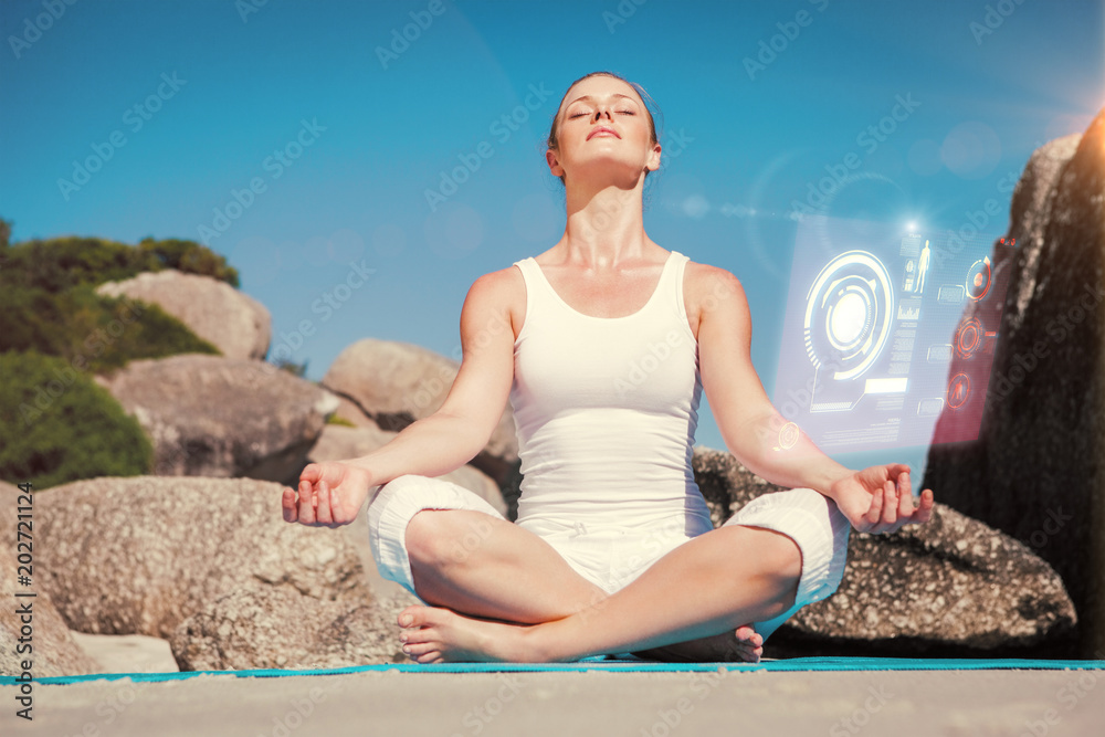 Blonde woman sitting in lotus pose on beach on mat against fitness interface