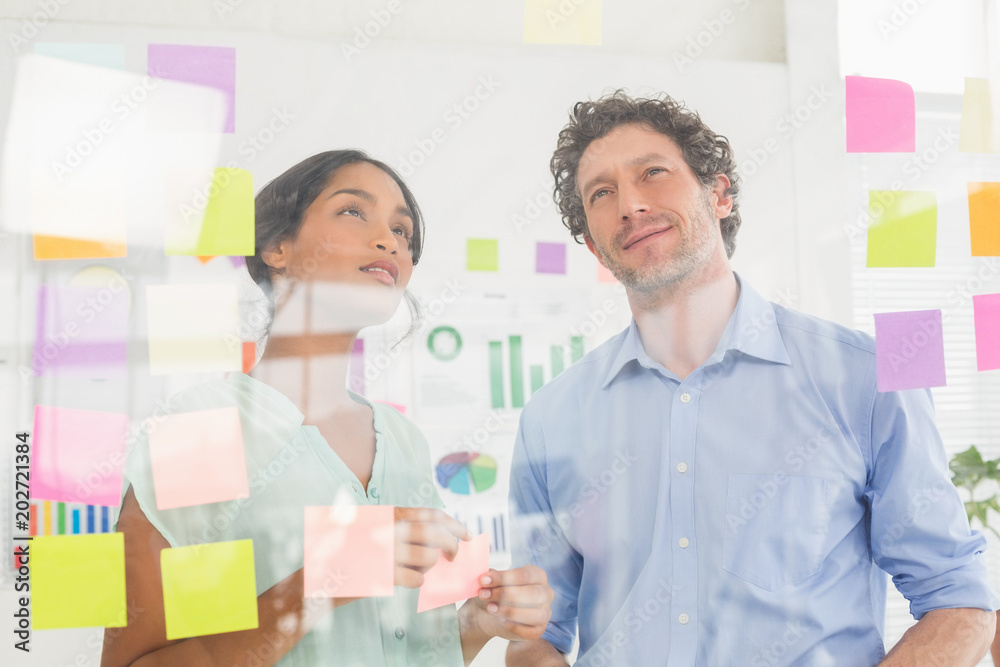 Puzzled business team looking post its on the wall Puzzled business team looking post its on the wall