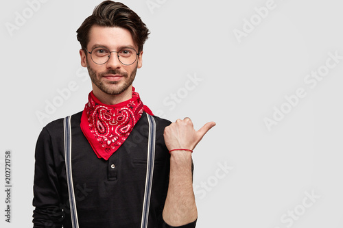 Confident serious fashionable male with trendy haircut, wears bandana and stylish black shirt, spectacles, poses against white background with copy space for your advertising content or promotion