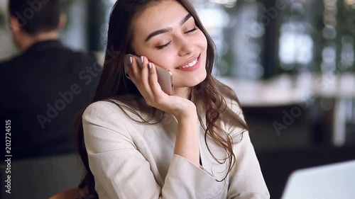 Beautiful business girl working on the phone at work on a laptop, enjoying the success. Conclusion of the contract, communication online. The modern woman is a freelancer working in a cafe