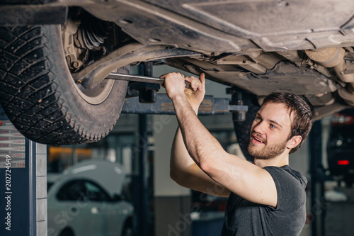 Auto mechanic working at auto repair shop under car with tool photo