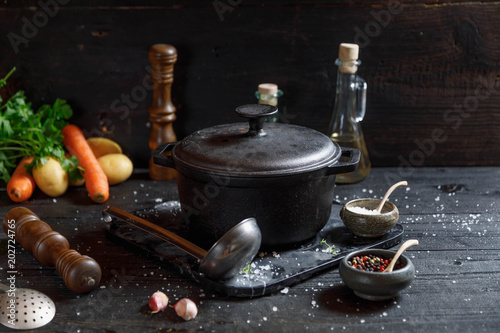 Old Cast iron pot and vegetables on dark wooden rustic table. Homemade food, cooking, vegetarian concept, copy space