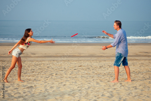 cheerful girl and man playing flying disk on the beach photo