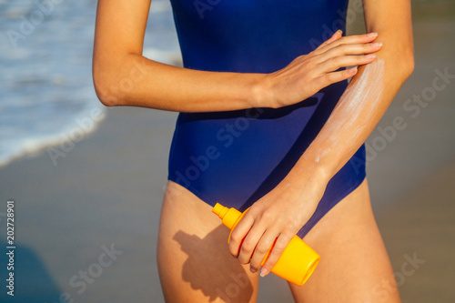 woman with a perfect figure applies a sunscreen spray on her hands on vacation