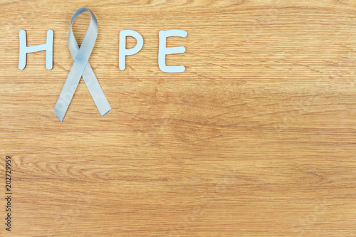 Oncological disease concept. Word "hope" written with the light blue ribbon as a symbol of prostate cancer in the corner of the wooden background.