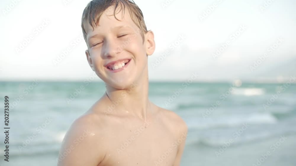 Close up, portrait of beautiful young teenage boy looking at camera smiling, tropical beach slow motion. Stock footage.