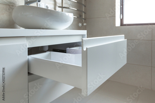 Opened U-shaped drawer in a bathroom furniture, white glossy front, handless design. 