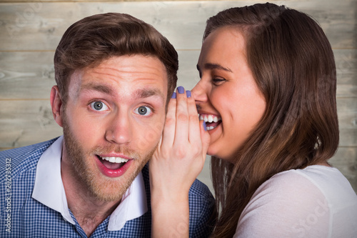 woman whispering secret into friends ear against bleached wooden planks background photo