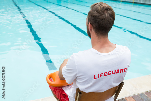 фотографія Lifeguard sitting on chair with rescue buoy at poolside