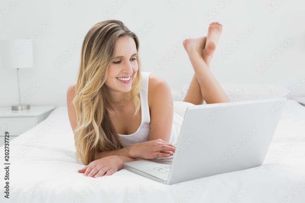 Pretty young woman using laptop in bed
