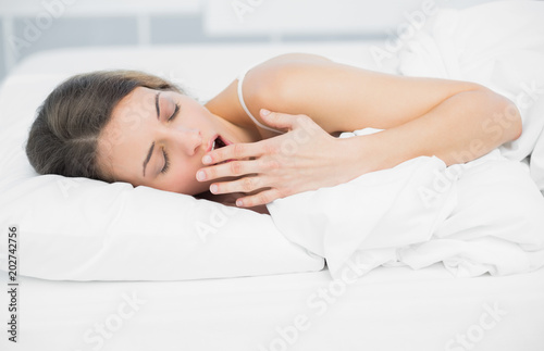 Tired attractive woman yawning while lying on her bed