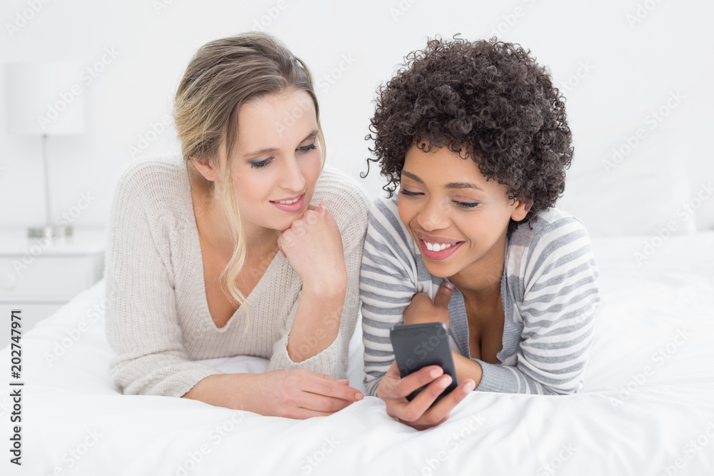 Smiling female friends reading text message in bed Smiling female friends reading text message in bed