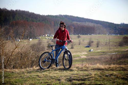 Beautiful young woman bathes in the rays of the spring sun on a hill above the river. Beautiful young woman with bicycle.