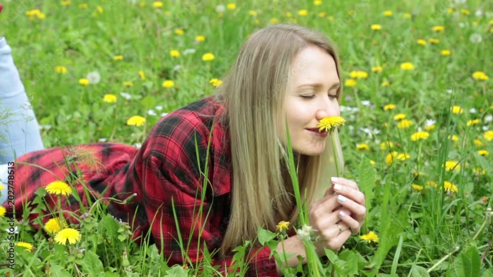 Young woman smelling a flower lying on a green grass.