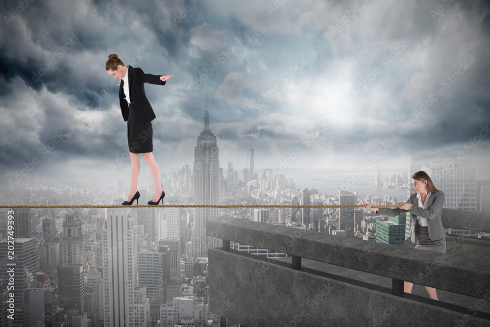 Young business woman pulling a tightrope for businesswoman against balcony overlooking city Young business woman pulling a tightrope for businesswoman against balcony overlooking city