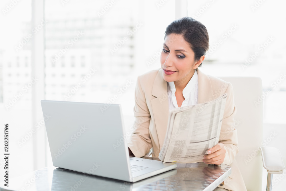 Happy businesswoman reading newspaper while working on laptop
