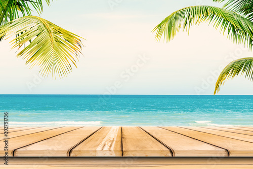 Empty wooden table and palm leaves background in summer time.