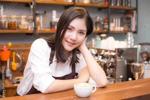 Asian women Barista smiling and looking to camera in coffee shop counter. Barista female working at cafe. Working woman small business owner or sme concept.