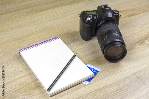 Notebook with pencils and SLR camera on wood texture photo