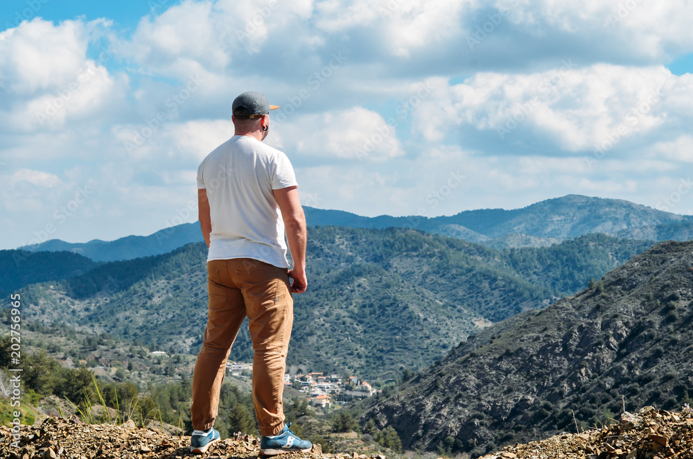Young man standing on top of cliff in summer mountains and enjoying view of nature. Hiking man standing and looking on mountains. Travelling and outdoor lifestyle concept. Copyplace, place for text Young man standing on top of cliff in summer mountains and enjoying view of nature. Hiking man standing and looking on mountains. Travelling and outdoor lifestyle concept. Copyplace, place for text