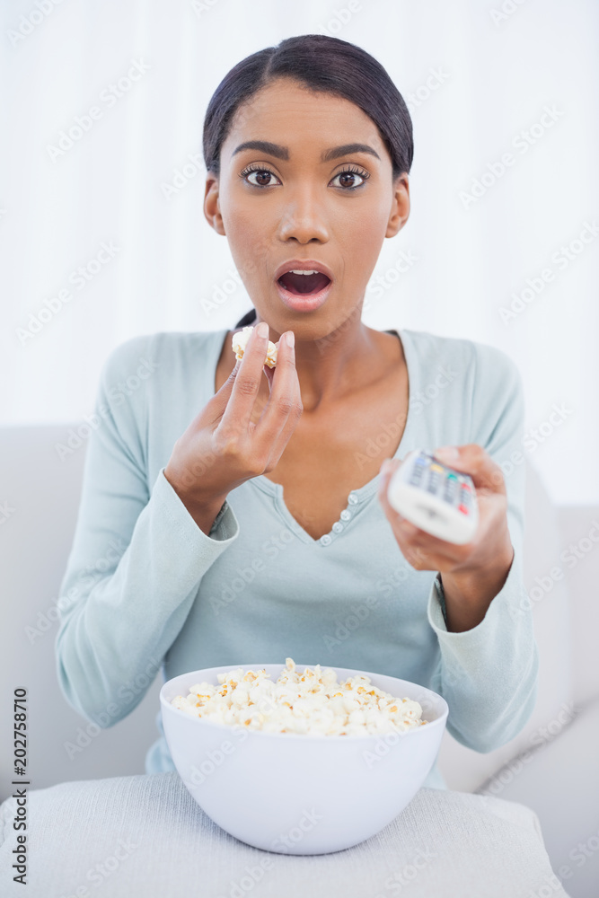 Astonished attractive woman eating popcorn while watching tv Astonished attractive woman eating popcorn while watching tv
