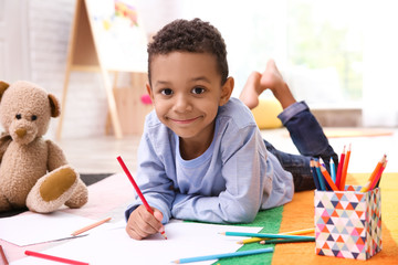 Little African-American boy drawing on floor indoors