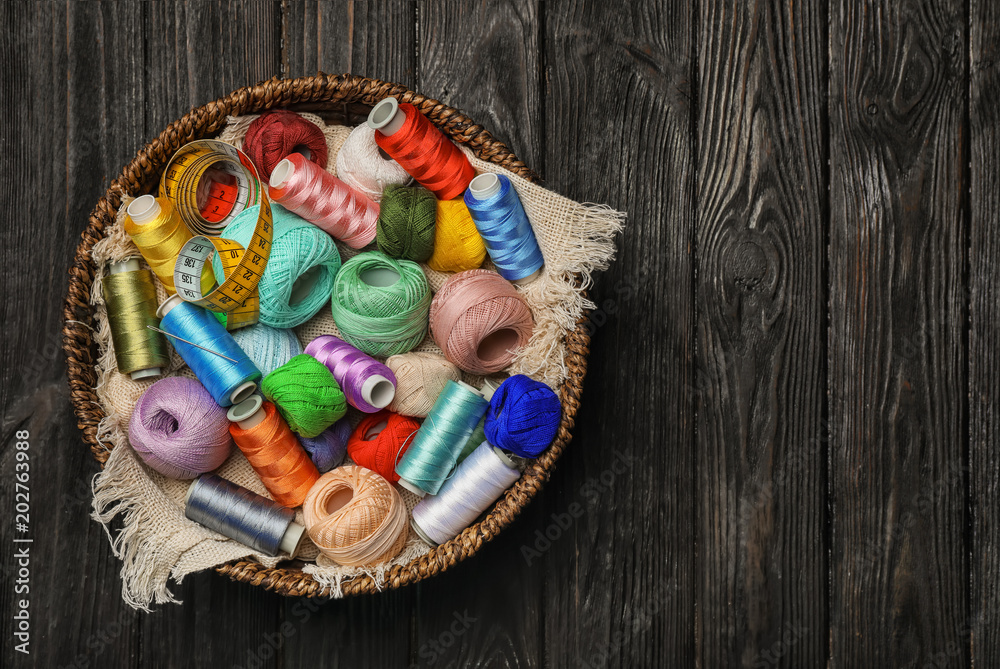Basket with color sewing threads on wooden background, top view