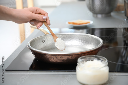 Woman putting coconut oil on frying pan in kitchen, closeup
