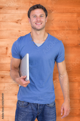 Smiling man with closed laptop against wooden planks © vectorfusionart