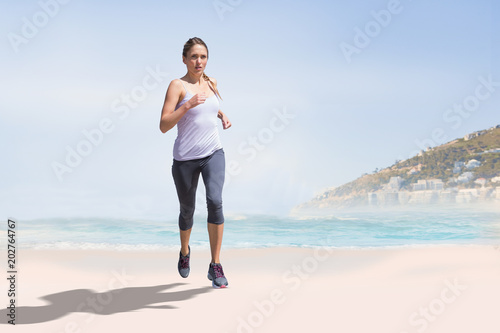 Focused fit blonde jogging against beautiful beach and blue sky